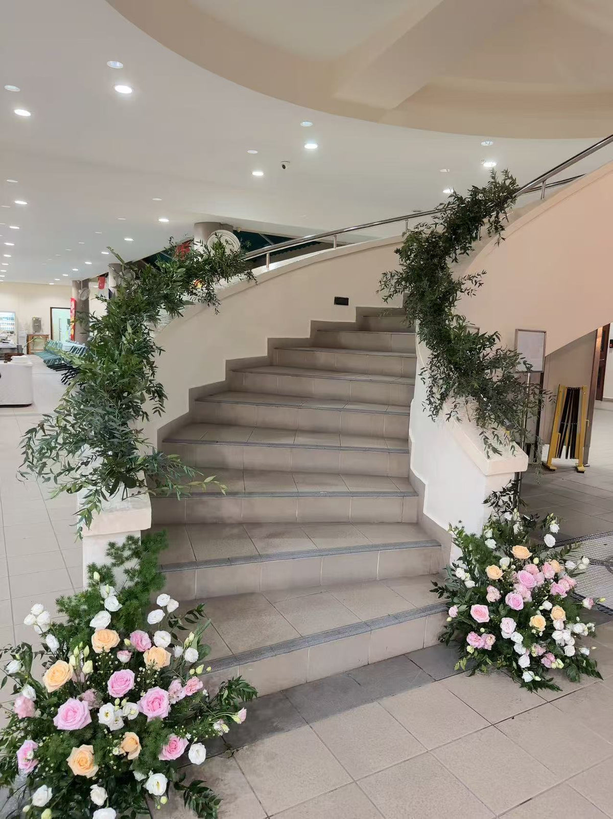 Grand curved staircase framed with greenery garlands and lush floor floral arrangements